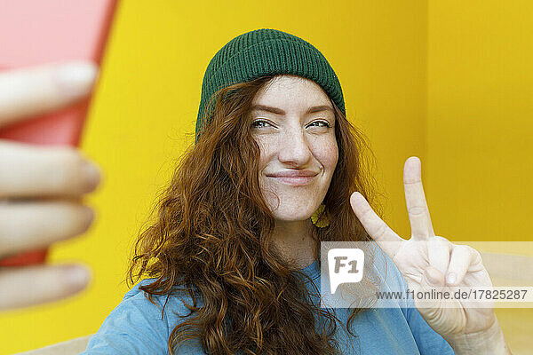 Smiling woman green wearing knit hat taking selfie through smart phone at home