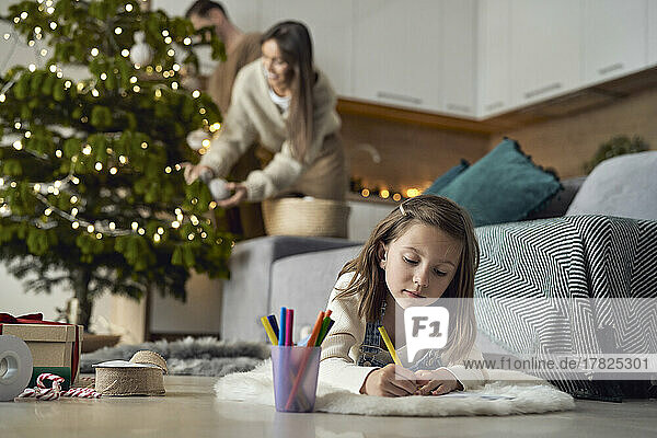 Girl writing letter to Santa Claus with parents in background at home