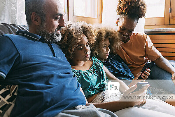 Parents looking at children using smart phones sitting on sofa