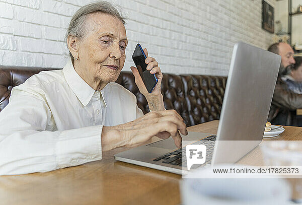 Ältere Frau mit Smartphone und Laptop im Café