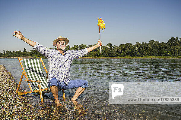 Smiling man with arms outstretched holding paper pinwheel toy at riverbank