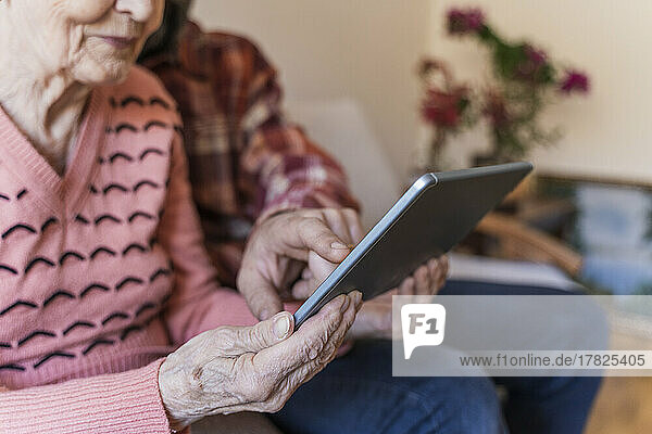 Mature man teaching tablet PC to senior woman at home