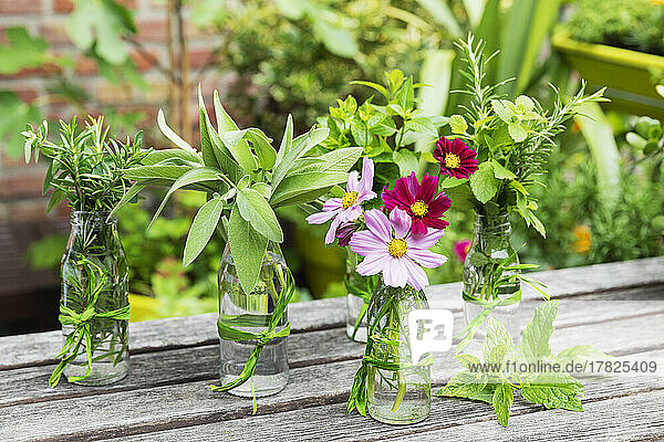 Fresh herbs and flowers in decorated glass bottles standing on balcony table