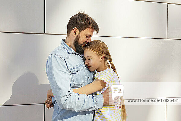 Smiling man embracing daughter in front of wall