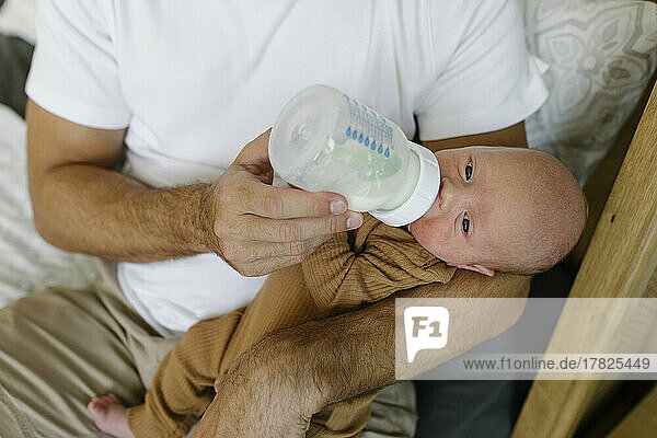 Man feeding milk to baby boy with bottle at home