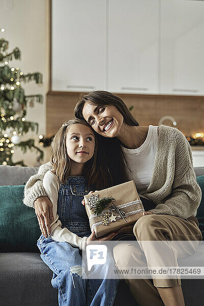 Glückliche Frau mit Weihnachtsgeschenk umarmt Tochter im Wohnzimmer