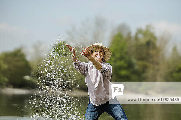 Cheerful mature woman playing with water on sunny day