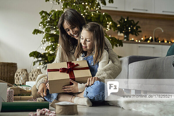 Girl holding Christmas present sitting with mother on floor at home