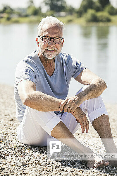 Smiling man wearing eyeglasses sitting at riverbank