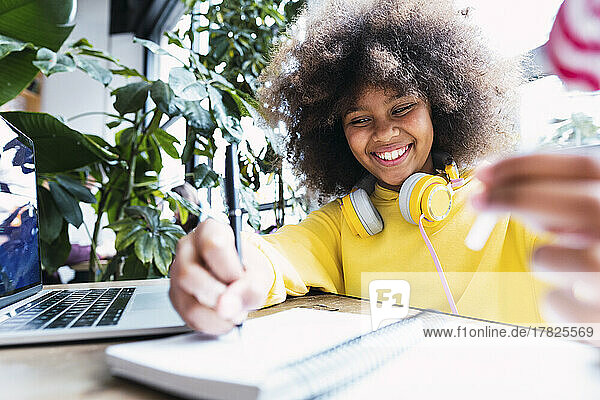 Lächelndes Mädchen macht Hausaufgaben am Laptop am Tisch im Café