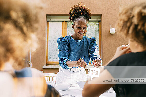 Smiling woman serving food to children at dining table