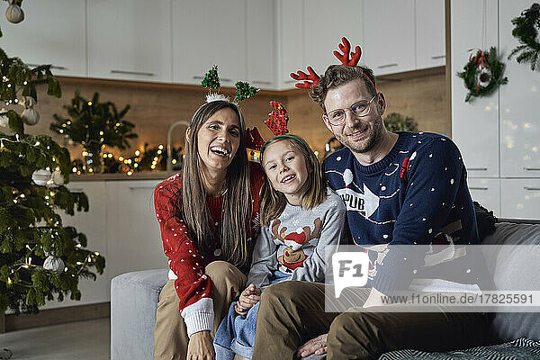 Happy family wearing Christmas antler sitting on sofa at home