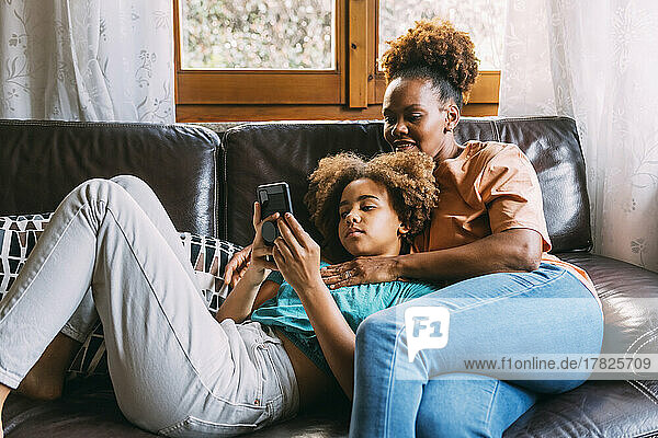 Girl sharing smart phone with mother on sofa at home