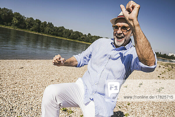 Happy senior man dancing at riverbank on sunny day