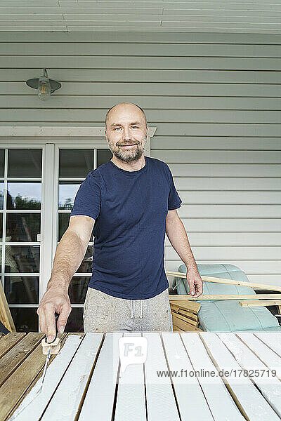 Smiling mature man painting planks in back yard