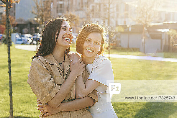 Glückliche Frau umarmt fröhliche Freundin im Park an einem sonnigen Tag