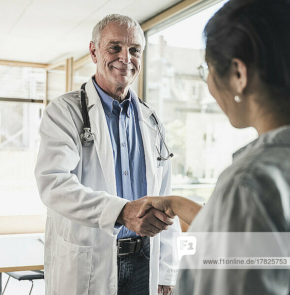 Smiling doctor shaking hand with patient in medical clinic