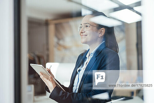 Smiling businesswoman with tablet PC looking through window