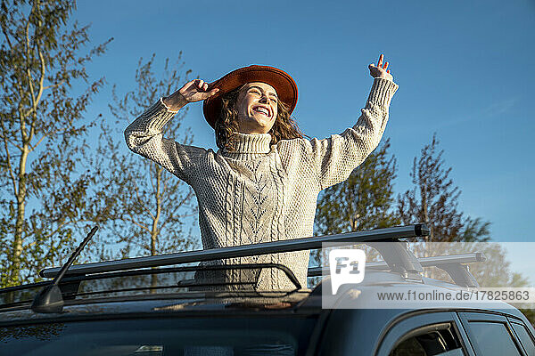 Fröhliche Frau mit Hut genießt es durch das Sonnendach des Autos