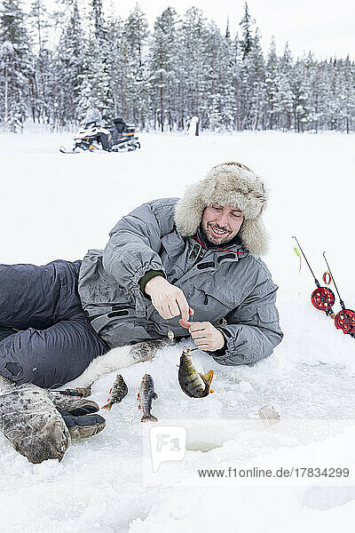 Fröhlicher Mann  der den Fischfang aus dem Eisloch aufnimmt  Lappland  Schweden  Skandinavien  Europa