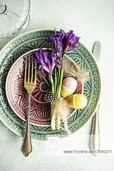 Ostergedeck mit Keramiktellern  Iris  Eiern und Federn auf Betontisch