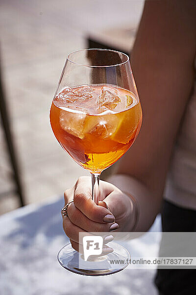 Hand holding stemmed glass with Aperol Spritz