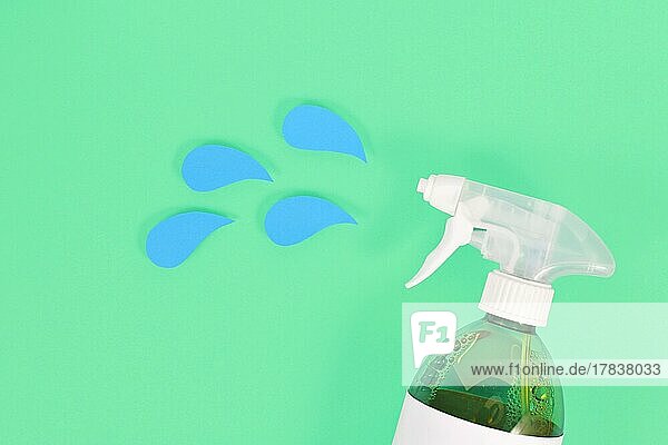 Grüne Reinigungsmittel-Sprühflasche mit blauen  aus Papier ausgeschnittenen Flüssigkeitstropfen