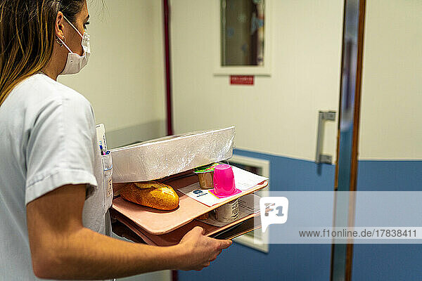 Caregiver carrying meal trays for patients in hospital.
