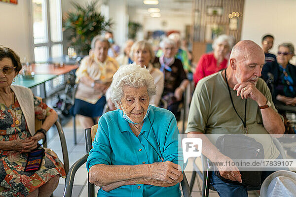 Seniors sitting in chairs or wheelchairs attending a music concert in a retirement home.