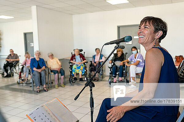 Seniors sitting in chairs or wheelchairs attending a music concert in a retirement home.