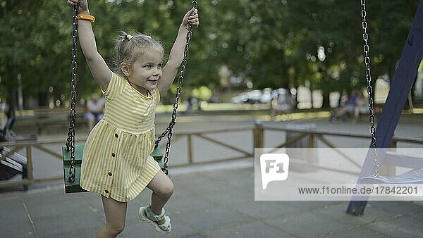 Nettes kleines Mädchen reitet auf einer Schaukel auf dem Spielplatz. Kind Mädchen spielen auf dem Spielplatz im Stadtpark. Odessa Ukraine Europa