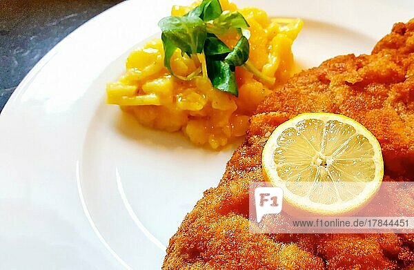 Delicious golden-brown fried Wiener Schnitzel with potato salad and a slice of lemon on a white plate