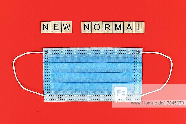 Flat Lay mit blauen Einweg Schutzmaske und hölzernen Buchstaben bilden Worte neue normale auf rotem Hintergrund