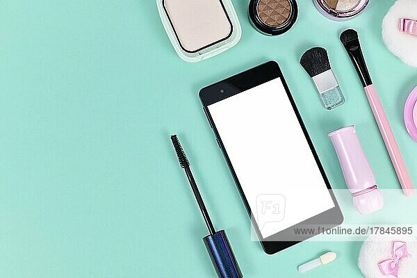 Flat Lay mit leeren schwarzen Smartphone mit leeren weißen Bildschirm von Make up Beauty Produkte auf hellgrünem Hintergrund mit Kopie Raum auf der linken Seite umgeben