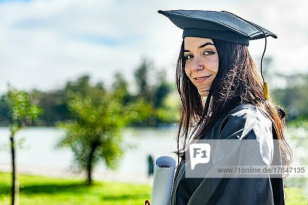Glückliches kaukasisches Mädchen mit langem braunem Haar  das ein Diplom hält und in die Kamera schaut