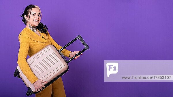 Attraktive glückliche Reisende  die ihren Koffer wie eine Gitarre vor einem lila Hintergrund hält. Raum kopieren