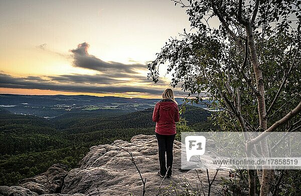 Woman in red standing on a rock watching the sunrise  Elbe Sandstone Mountains  Dresden  Germany  Europe