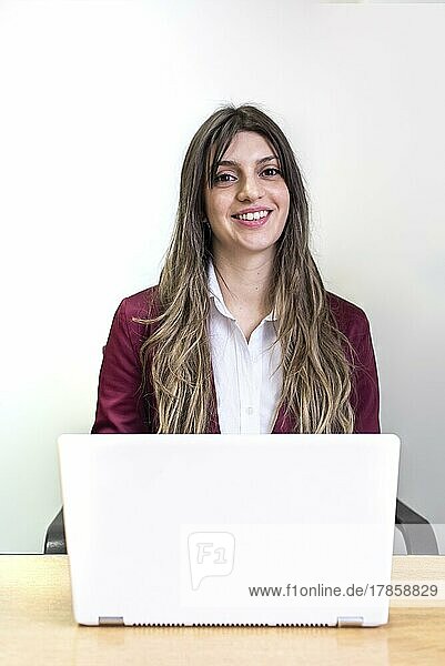 Beautiful smiling woman working on her white laptop while looking at camera