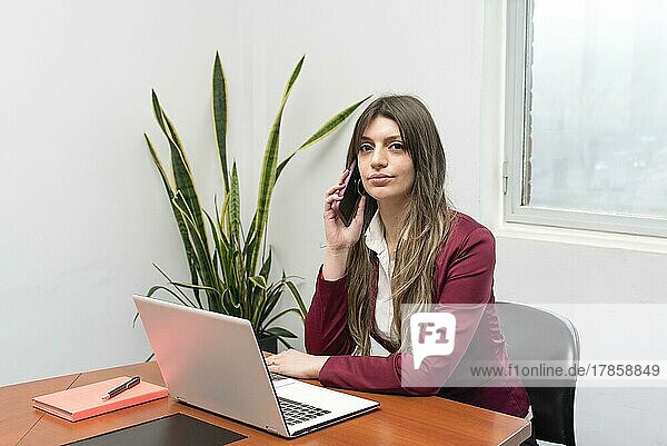 Beautiful woman working on her laptop while she is talking on the phone in the office