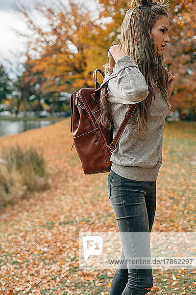 woman adjusting backpack outside in the fall surrounded by orang