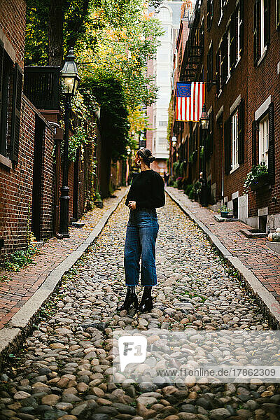Woman on cobblestone road with American flag from brick townhouse