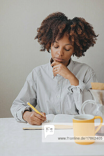 A curly haired woman takes notes in a notebook in the kitchen.