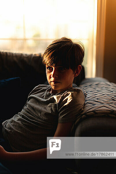 Boy sitting on couch in warm evening window light at home.