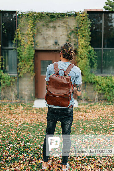 man wearing man bun and backpack looking at old building with vi
