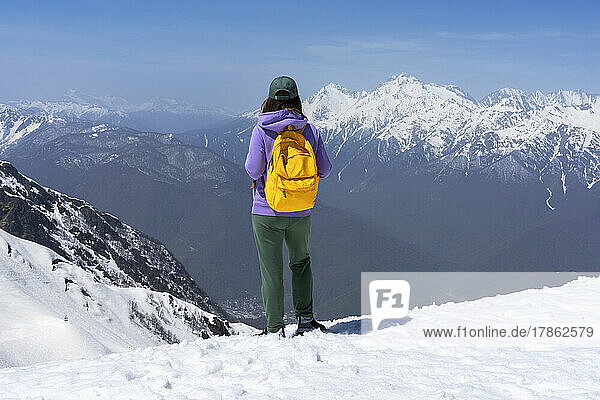 Young woman with yellow backpack lookind at view of snowy mountains