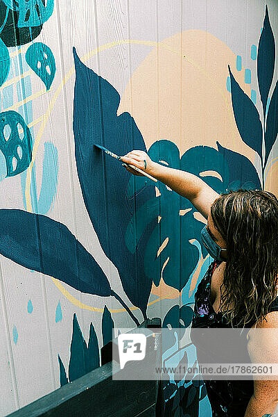 female artist painting a mural on wall of local business