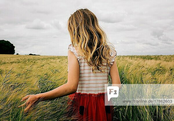 girl walking through a corn field feeling the grass on a cloudy day