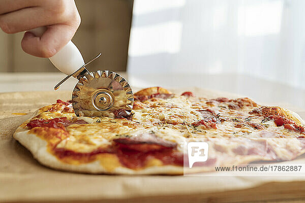 A hand with a pizza knife cuts a pizza close-up.