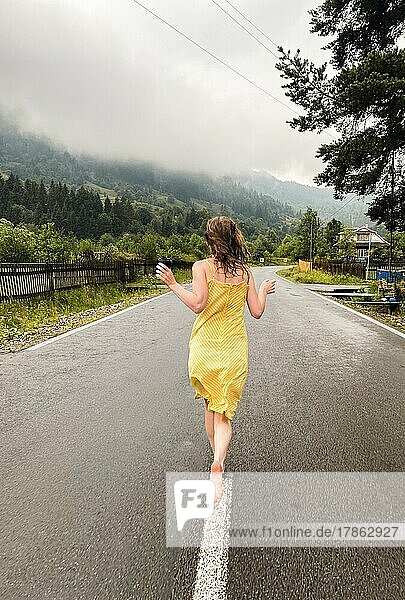 A woman in a yellow dress runs along the road in the rain