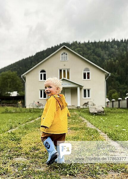 A toddler in a yellow raincoat near the house.